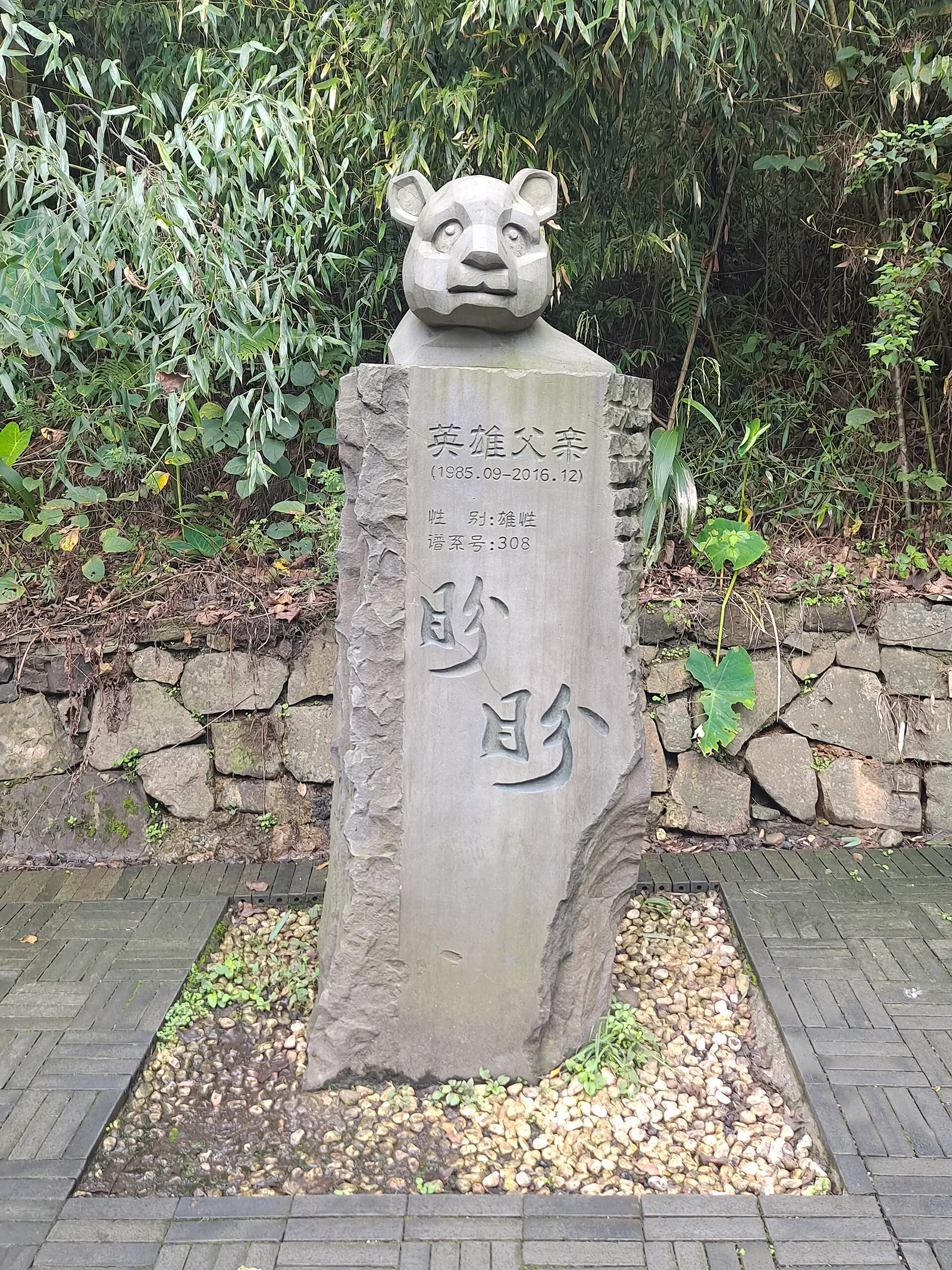 Dujiangyan Panda Base: stone panda sculpture on a rock marker among greenery