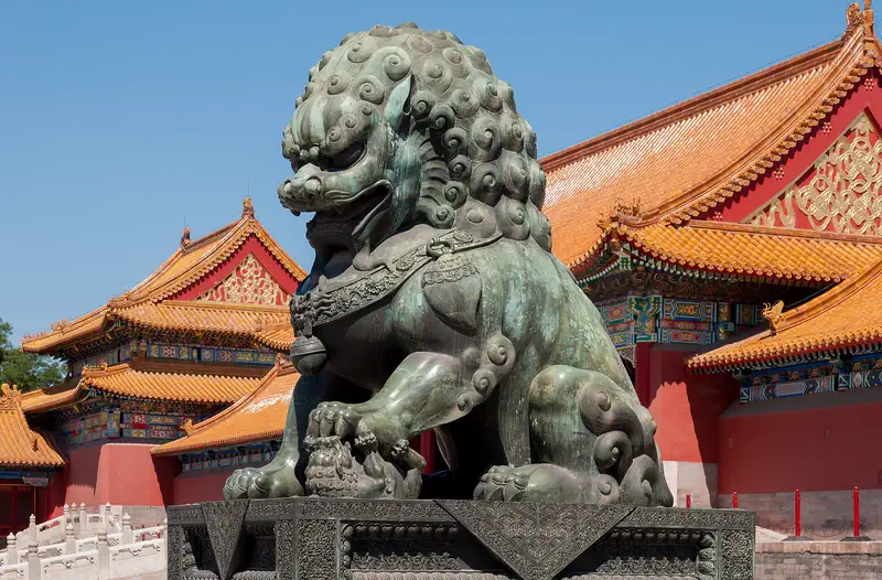 Forbidden City: bronze guardian lion before red walls and yellow-tiled roofs at the Gate of Supreme Harmony
