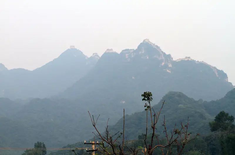 Great Wall: hazy wooded mountain ridgeline with a bare branch in the foreground