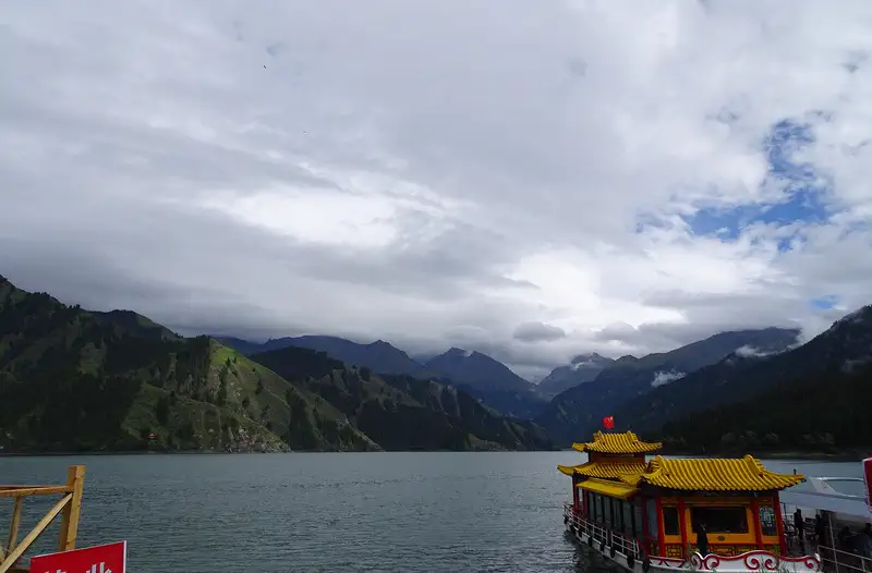 Heavenly Lake (Tianchi): a tour boat on the dark alpine lake below forested slopes and cloud-covered peaks