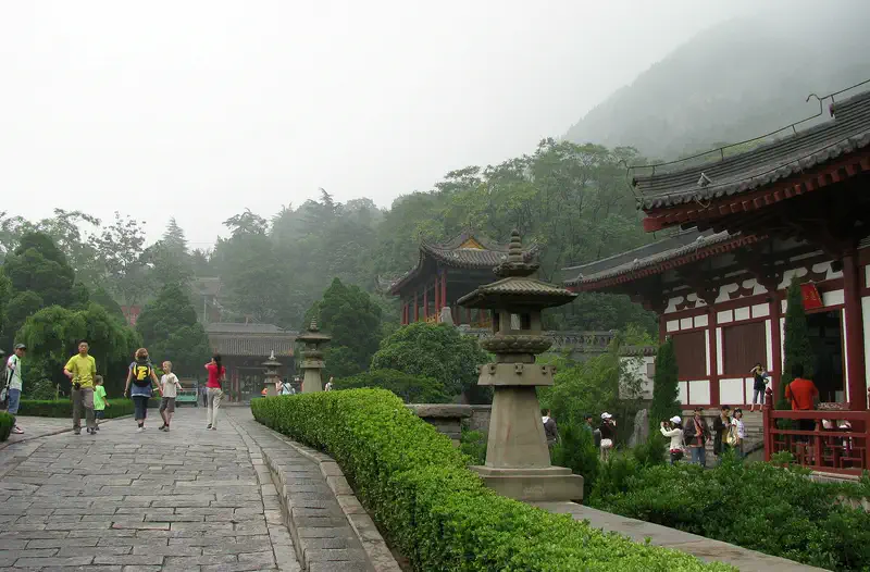 Huaqing Palace and Hot Springs: stone pathway lined with hedges leads past pavilions and a stone lantern toward misty hills