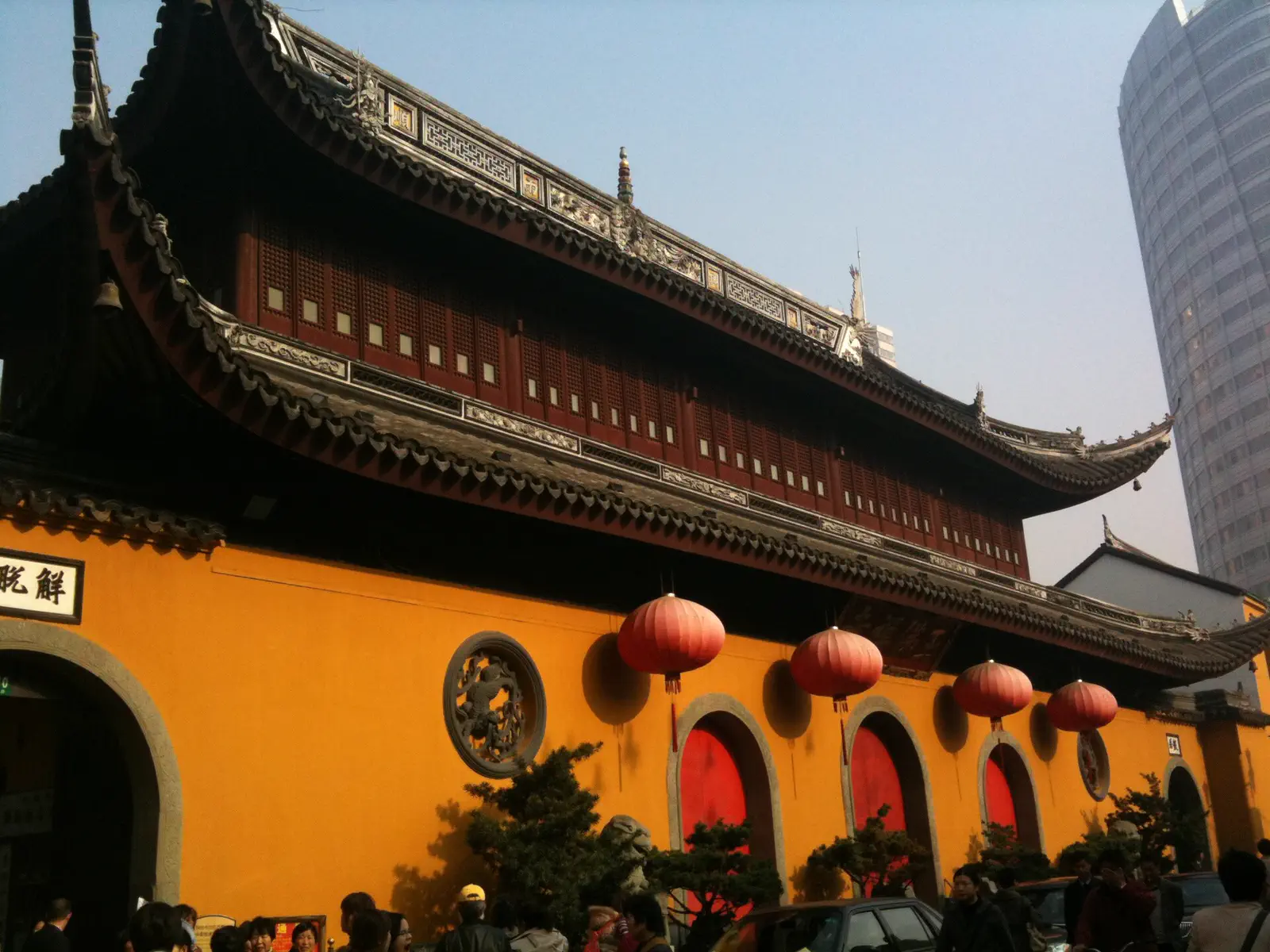 Jade Buddha Temple: ochre exterior wall with red lanterns, dark tiled roofline, and a modern skyscraper behind