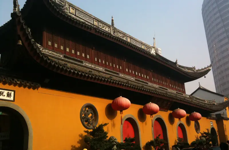 Jade Buddha Temple: ochre exterior wall with red lanterns, dark tiled roofline, and a modern skyscraper behind