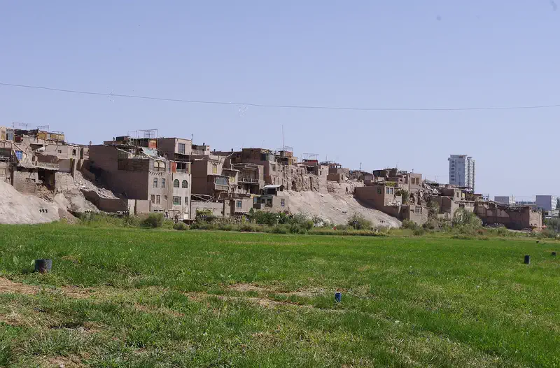 Kashgar Old City: distant view of mud-brick buildings on a hillside beyond a green field