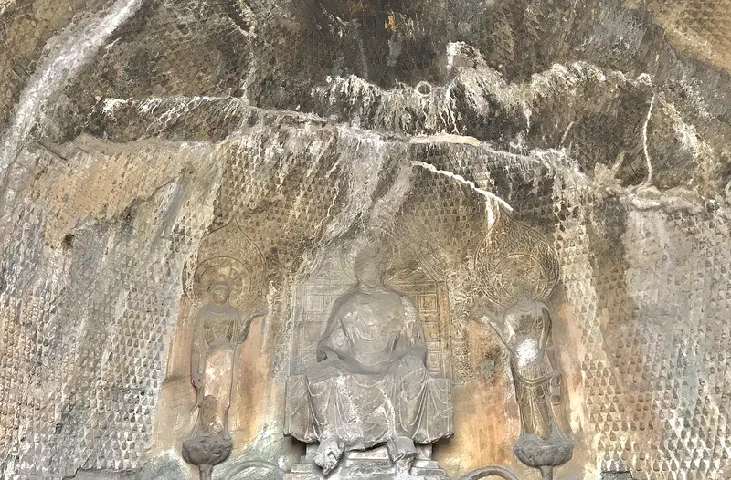 Longmen Grottoes: weathered Buddhist figures carved into a water-stained limestone niche