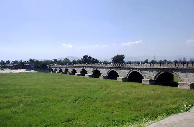 Lugou (Marco Polo) Bridge: long stone arch bridge crossing a grassy field under a clear blue sky