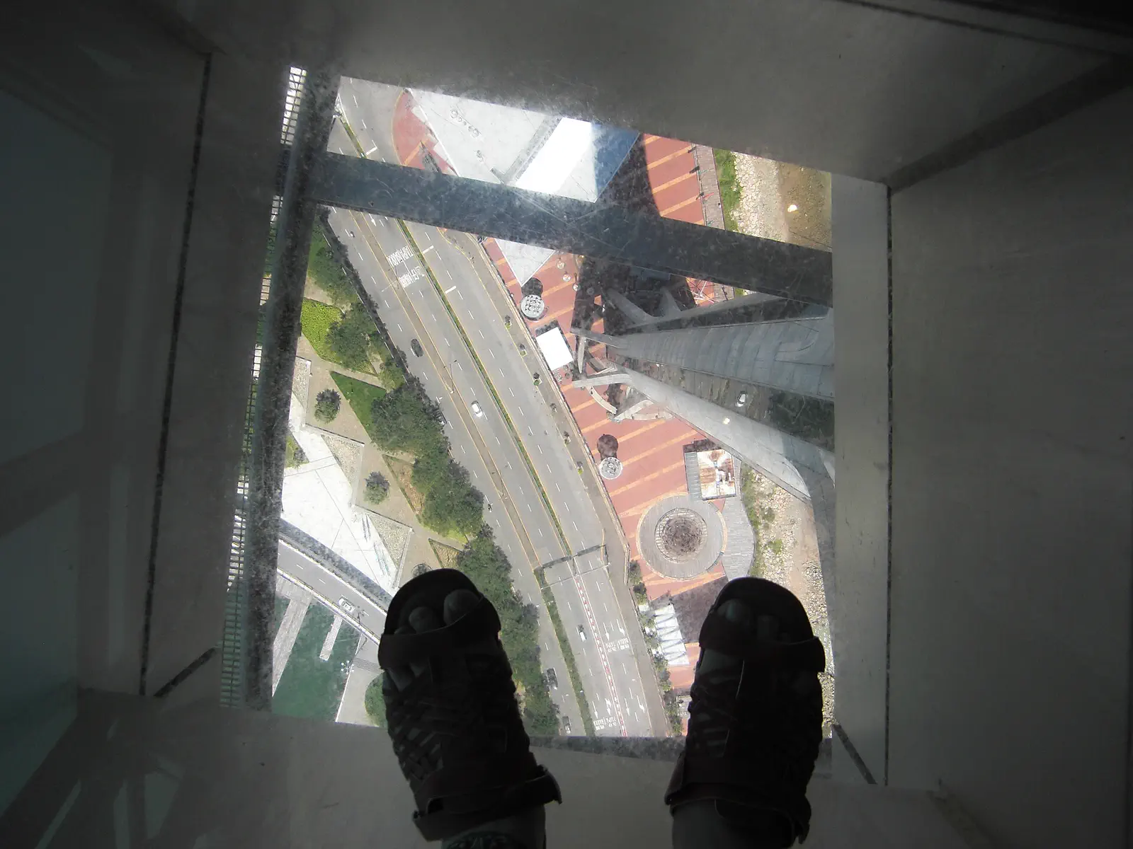 Macau Tower: view straight down through a glass floor to the street far below, with two feet visible