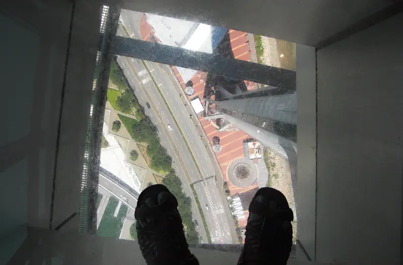 Macau Tower: view straight down through a glass floor to the street far below, with two feet visible