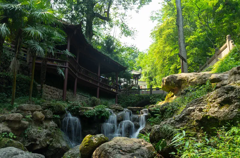 Mount Qingcheng: green hillside garden with a small waterfall, mossy rocks, and a wooden pavilion roof