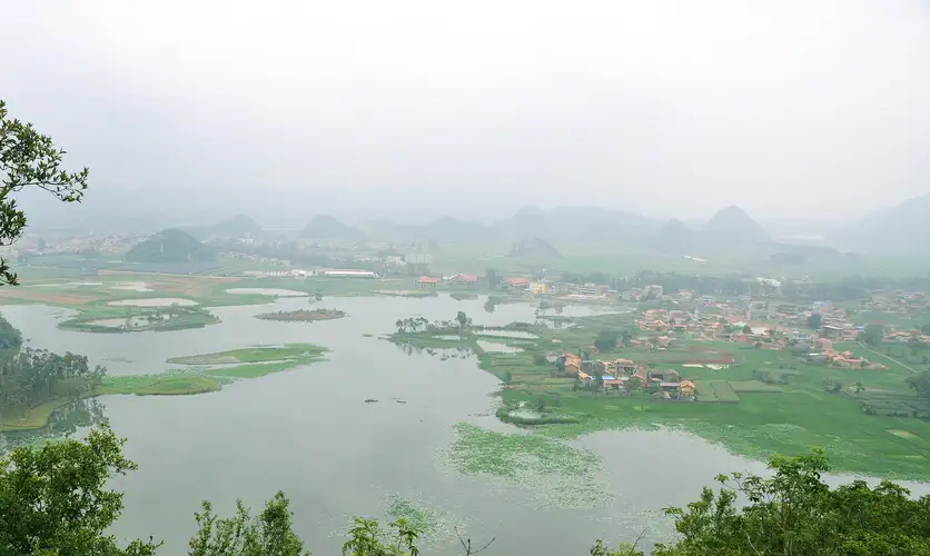 Puzhehei: misty karst hills surround a lake and green fields dotted with a small village