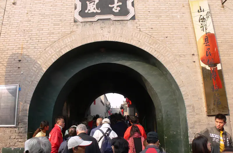 Qiao Family Compound: crowd of visitors walking through a stone archway entrance below carved signage