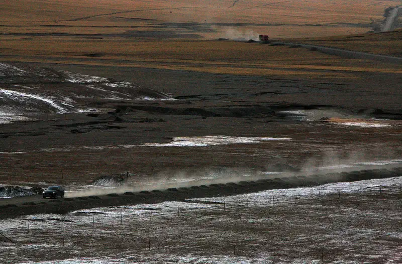 Hoh Xil: open, near-empty plateau with low hills and a dust trail crossing it