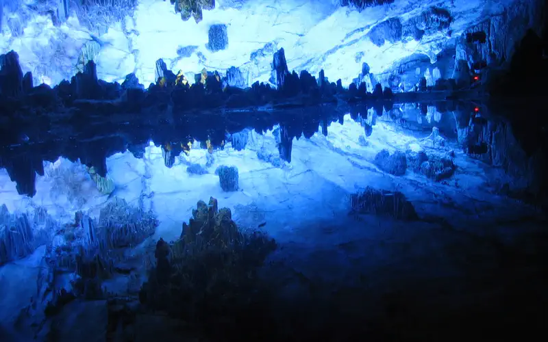 Reed Flute Cave: illuminated cave interior with rock formations lit in blue, reflected in still water