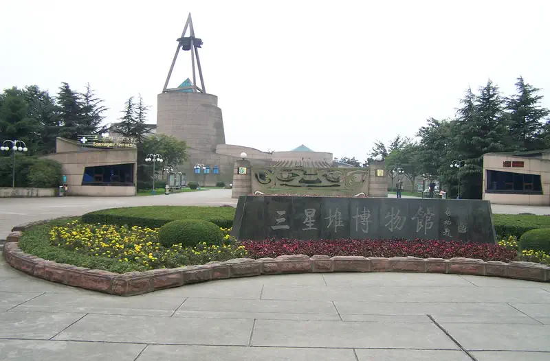 Sanxingdui Museum: outdoor plaza with a tall triangular sculpture beside an inscribed stone marker and trees