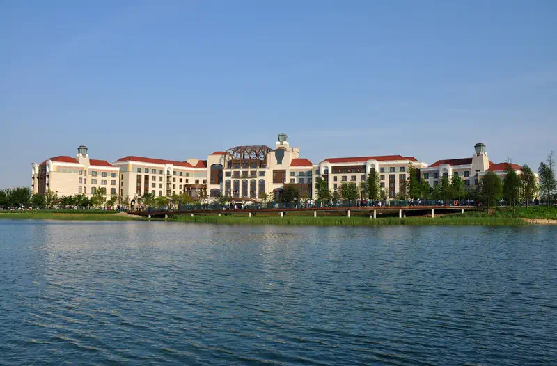Shanghai Disneyland: castle-like building with turrets and red roofs beside a lake reflecting the structure