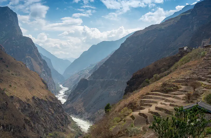 Three Parallel Rivers: a river cutting through a deep gorge with terraced slopes and hazy ridges beyond