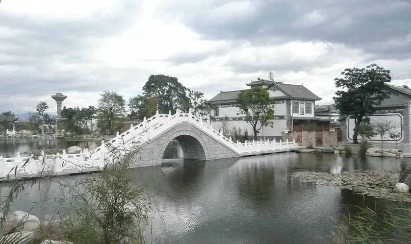 Xizhou (Bai minority town): white stone arch bridge over water beside white-walled buildings, under a cloudy sky