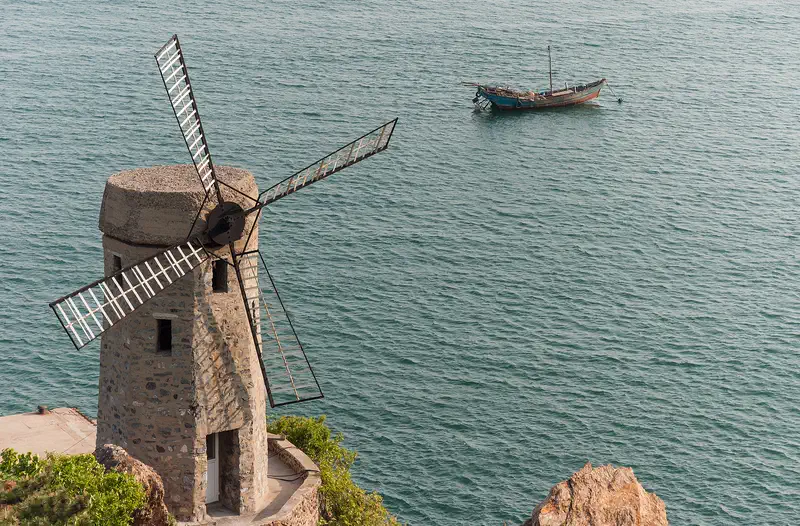 Dalian: a stone windmill on the shore of Xinghai Bay with a boat out on the water