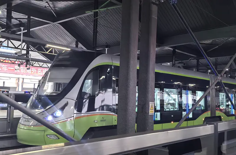 Foshan: green light rail train parked under a covered station shed