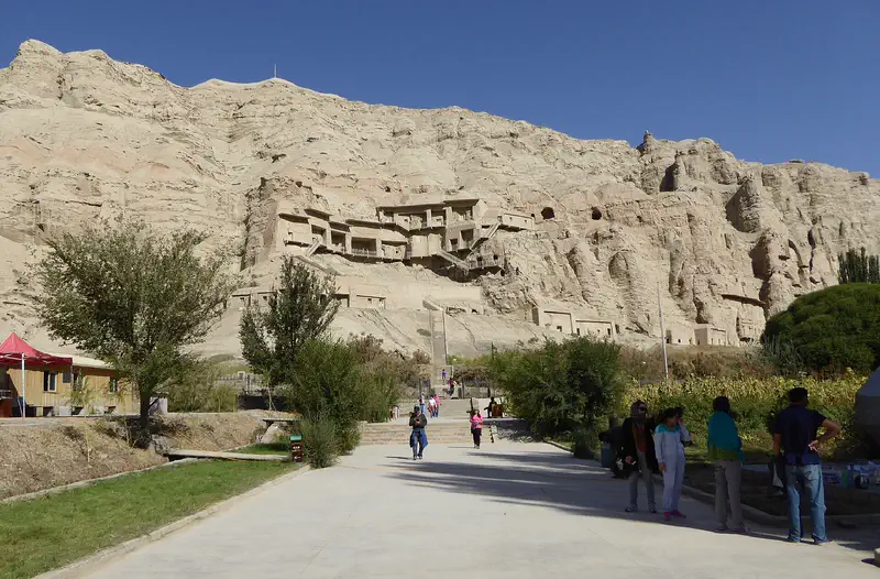 Kuqa: the cliff face of the Kizil Caves above a tree-lined path
