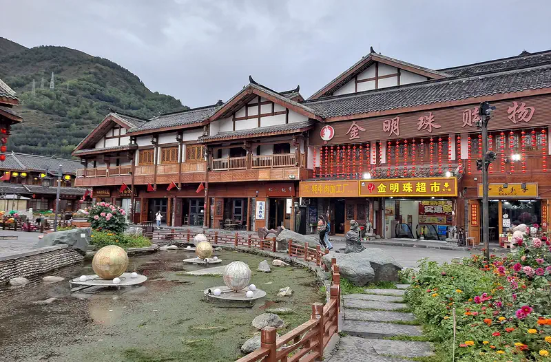 Songpan: traditional wooden buildings along a street with a small pond and flowers