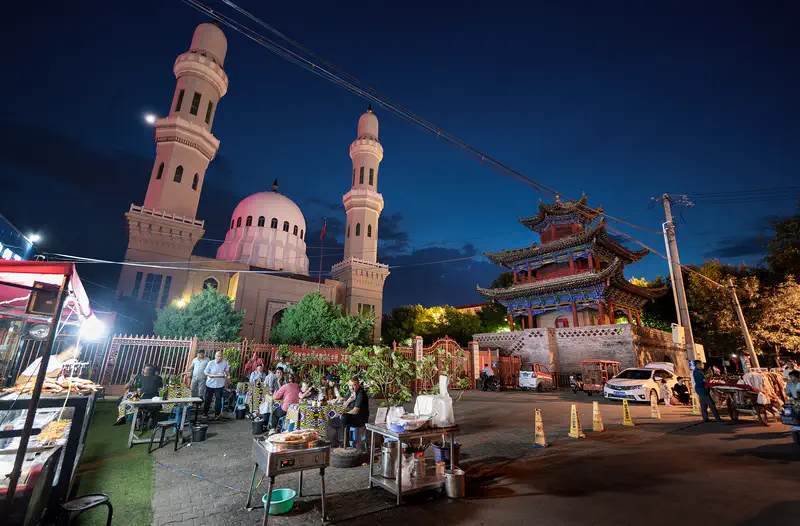 Yining: the twin minarets of Batul Mosque lit at night above a street market