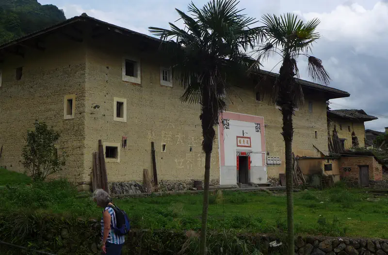 Yongding: a rammed-earth Hakka tulou with a tiled roof, palm trees in front