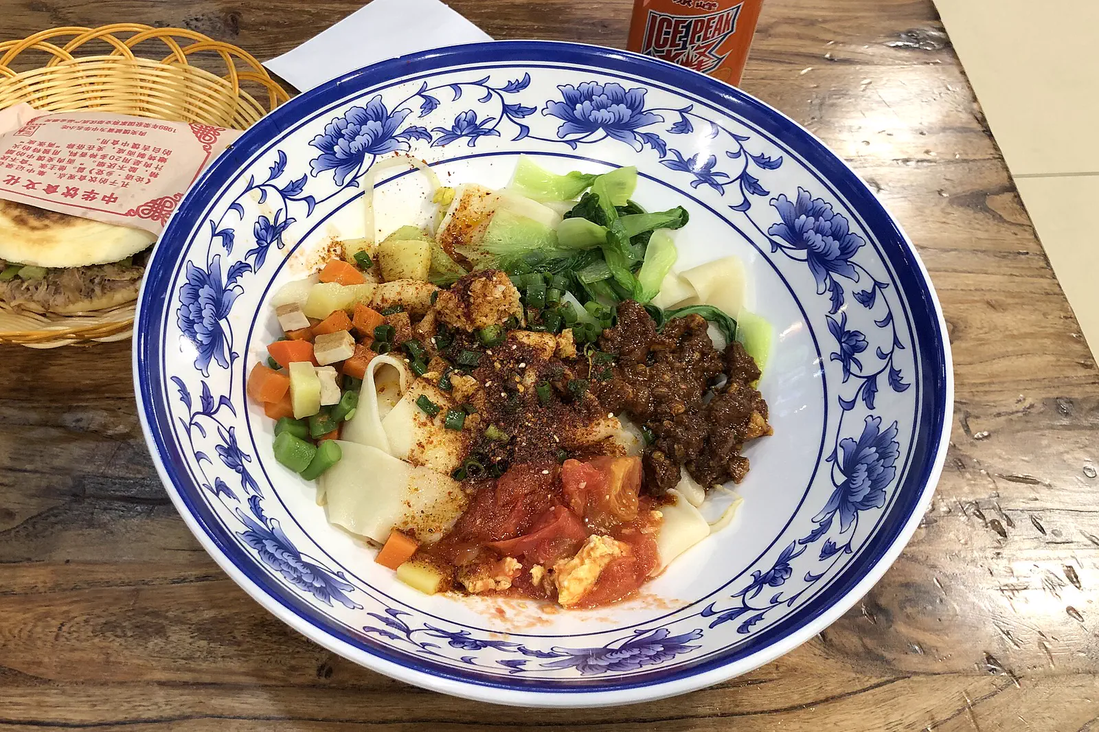 Biangbiang Noodles: wide hand-pulled noodles topped with minced meat, tomato, greens and chilli in a blue-and-white bowl